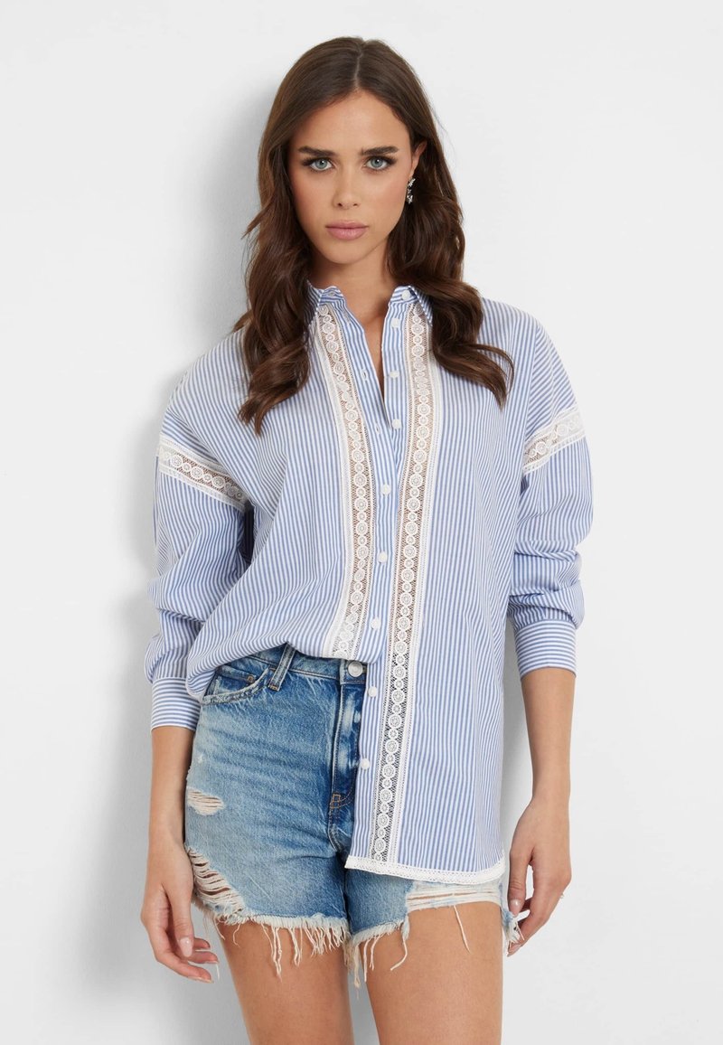 Camicia a righe blu con pizzo bianco, apertura con bottoni sul davanti e maniche arrotolate, abbinata a pantaloni shorts in denim strappati.