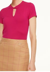 Fuksjowa bluzka z krótkim rękawem z dekoltem w kształcie łezki, w połączeniu z beżową spódnicą w kratkę z różowymi przeszyciami i boczną kieszenią.