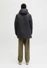 Ciemnoszary ocieplany płaszcz z kapturem, z poziomym pikowaniem i elastycznymi mankietami, w zestawieniu z oliwkowozielonymi spodniami o luźnym fasonie.