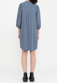 Abito blu lunghezza ginocchio con fantasia a pois, maniche a sbuffo, scollatura rotonda e vestibilità morbida. Indossato con stivaletti neri alla caviglia.