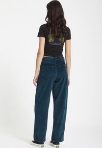 Teal corduroy bukser med brede ben, to baglommer og høj talje. Sæt sammen med en sort cropped t-shirt med farverige grafik.