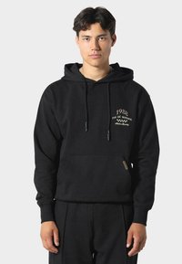 Czarna bluza z kapturem wykonana z miękkiego materiału, z kieszenią kangurka, troczkami przy kapturze oraz haftowanym napisem na piersiach. Luźny krój.