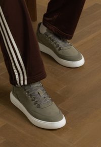 Gray sneakers with textured upper, white sole, and gray laces. Paired with brown pants featuring white stripes along the sides.