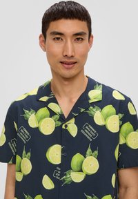 Korte mouwen marineblauw shirt met een limoen- en bladerenpatroon, knoopsluiting aan de voorkant en een kraag. Stof lijkt lichtgewicht en heeft een gladde textuur.