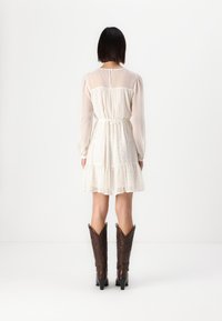 Cream-colored dress with sheer sleeves and gathered waist, featuring a ruffled hem. Worn with brown cowboy boots.