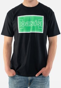 Black cotton t-shirt featuring a large green "oasis" graphic with a white border. The fit is relaxed, with short sleeves and a crew neckline.