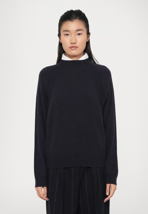 Maglione blu scuro realizzato in tessuto morbido, con collo alto e maniche raglan. Abbinate a una camicia bianca con colletto e pantaloni a righe nere.