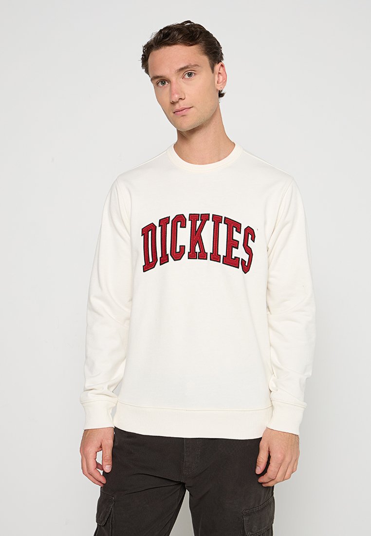Felpa color crema con maniche lunghe e scollo a girocollo lavorato a maglia. Logo "DICKIES" ricamato in rosso sul petto. Tessuto misto cotone.