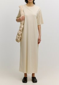 Beige maxi-jurk met korte mouwen, eenvoudige ronde halslijn en een ontspannen pasvorm. Accessoires bestaan uit een geknoopte beige tas en zwarte instappers.