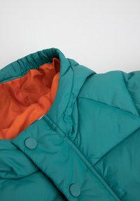 Tyrkysová prošívaná bunda s oranžovým podšívkou, s kapucí, zapínáním na knoflíky a prošívaným vzorem. Měkká, hladká textura.