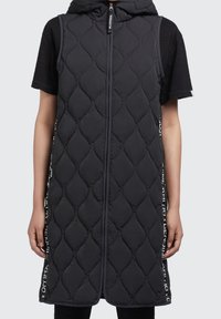 Black quilted sleeveless vest with a hood, featuring a zip front and side logo accents. The fabric has a smooth texture and elongated shape.