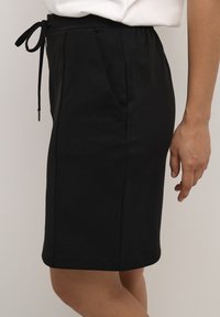 Jupe noire à taille élastique avec cordon de serrage ajustable, dotée de poches latérales élégantes et d'une coupe droite, fabriquée en tissu lisse.