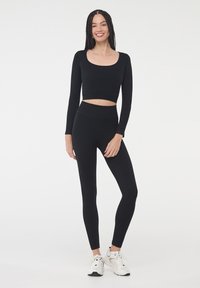 Czarny, długi rękaw, krótki top i legginsy o wysokim stanie z gładkiego, elastycznego materiału; noszone z białymi butami sportowymi.