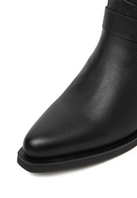 Czarne skórzane botki za kostkę z ostrym noskiem, gładką fakturą i wąskim paskiem wokół kostki. Płaska podeszwa z minimalną ilością detali.