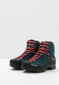 Fjellsko i mørk teal og svart, med røde snørebånd, røff såle, og vannavstøtende overdel med teksturerte detaljer. Merke: Salewa.