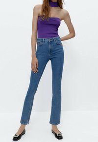 Fitted blå denimjeans med en lätt flare, hög midja och sidofåror i nederkant. Matchat med en lila off-shoulder topp och svarta platta skor.