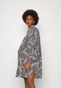 Vestido preto e branco com padr�ão, mangas longas, gola alta e fendas laterais. Feito de um tecido leve, apresenta uma silhueta solta e fluida.