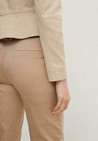 Beige cotton jacket with a tailored fit, featuring a slightly flared hem, and slim-fit beige pants with a discreet back pocket.