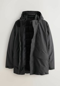 Sort, polstret jakke med hætte, lynlås foran, to store forlommer og et indre med quiltet foer. Blødt, vandtæt materiale.