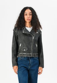 A black faux leather biker jacket with silver zippers, shoulder epaulets, a belted waist, and a textured finish, paired with blue jeans.