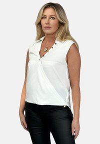 Biała bezrękawnikowa bluzka z dekoltem w kształcie litery V, z czarnymi guzikami metalowymi wzdłuż patki i złożonymi ramionami, co nadaje jej strukturalny wygląd.