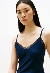 Canotta navy con scollatura a V, spalline sottili e delicati dettagli in pizzo lungo il collo e le spalline. Tessuto morbido ed elasticizzato.