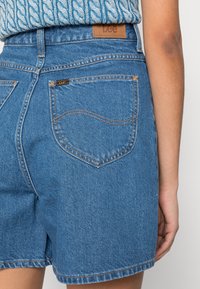 Vaaleansiniset farkkushortsit, joissa on teksturoitu viimeistely, nahkainen "Lee"-etiketti, näkyvät ompeleet ja kaksi takataskua.