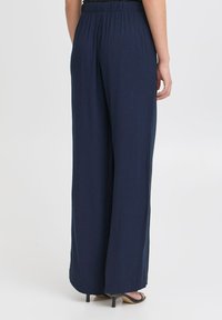 Kalhoty s širokými nohavicemi v námořnické modři s elastickým pasem, z texturované tkaniny, s volným střihem, který dává volnost až ke kotníkům.