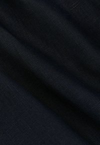 Gros plan sur un tissu noir avec une texture de tissage visible et des plis doux créant des ombres et des reflets.