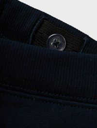 Col montant en sweat-shirt bleu marine avec texture côtelée et bande élastique. Présente un bouton en plastique transparent avec un design à quatre trous attaché à la ceinture intérieure.