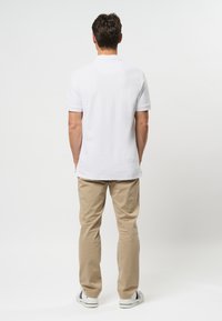 Polo blanc à manches courtes, associé à un chino beige et des baskets blanches, présentant un design simple et une coupe droite.