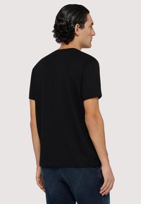 Svart bomullströja med korta ärmar och rundad halsringning, med en rak nederkant och en mjuk textur, bärs tillsammans med blå denimjeans.