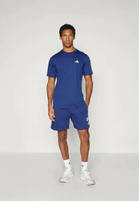 Zila sporta krekls un šorti, kas izgatavoti no viegla auduma, ar baltu logo uz krekla un šortiem. Vienkāršs dizains ar apaļu apkakli.