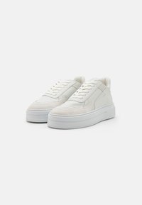 Baskets blanches avec un dessus en cuir lisse et des accents en daim, dotées d'une semelle blanche épaisse, d'un design à lacets et d'un col rembourré.