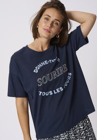Tricou din bumbac de culoare bleumarin, cu mâneci scurte, având un text multicolor "DONNE-TOI LE SOURIRE TOUS LES JOURS" brodat îngroșat.