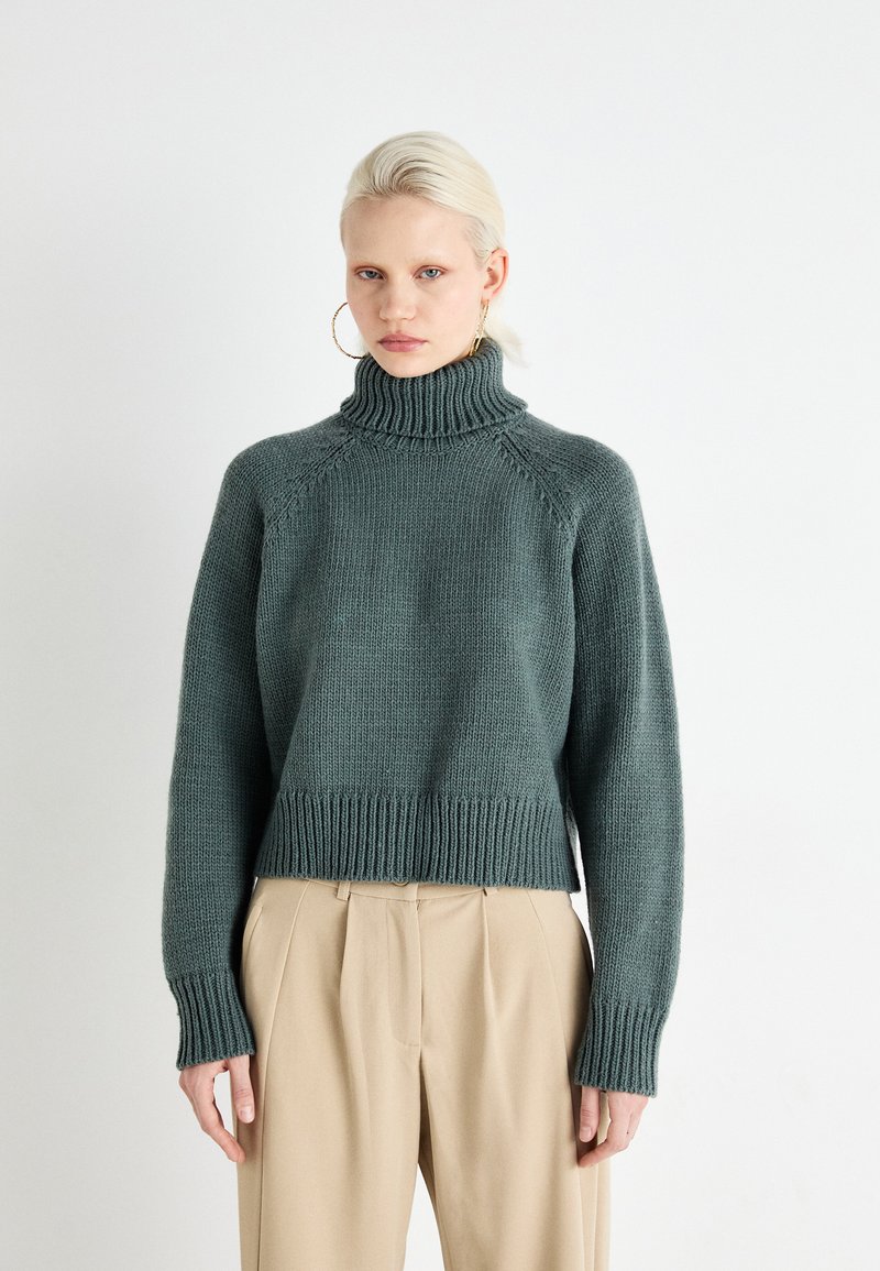 Knitted turtleneck sweater in dark green, featuring ribbed cuffs and hem, with a relaxed fit and textured fabric.