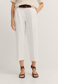 White tailored crop trousers with front pleats, a high waist, and side pockets. Paired with brown strappy sandals. Textured cream sweater.