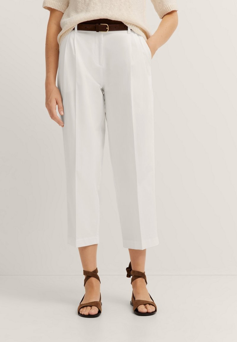 White tailored crop trousers with front pleats, a high waist, and side pockets. Paired with brown strappy sandals. Textured cream sweater.