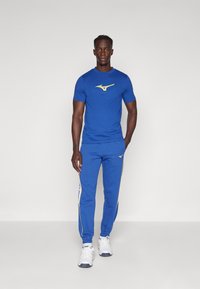 Blue athletic outfit featuring a fitted short-sleeve shirt with a yellow logo and matching sweatpants with yellow side stripes and logo accents.