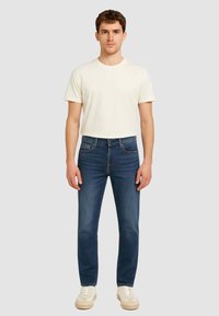 T-shirt chiara da uomo in crema e jeans slim-fit blu scuro; materiale di denim con cinque tasche, dotati di chiusura a bottone e zip.
