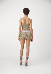 Brun og beige rutete crop top med tynne stropper, paret med en utsvingt, lagdelt miniskjørt og blå, stroppede høye hæler.