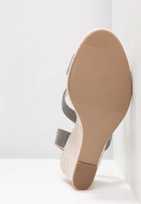 Sandale avec semelle en caoutchouc beige et talon compensé tissé, brides en tissu gris, photographiée de dessous sur fond blanc.