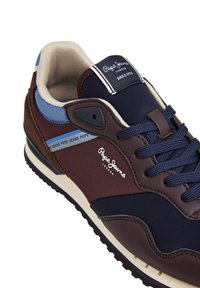 Meeste tennised tumesinises, pruunis ja sinises, millel on valged Pepe Jeans London logod külgedel ja keelel. Kingadel on tumesinised paelad ja pehme krae.