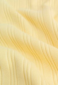 Dzeltens ribots audums ar gludu, mīkstu tekstūru un vertikālām līnijām, kas ataino vienmērīgas krokas un maigas locītes.