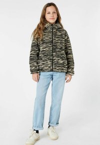 Fleecejack in beige en zwart zebra-patroon, met een hoge kraag en ritsluiting. Gepaard met lichtblauwe jeans en witte sneakers.