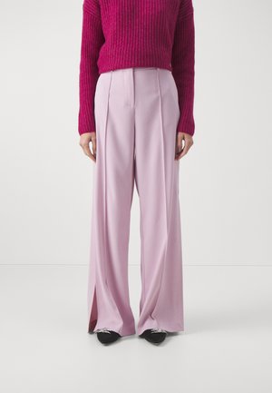 Pantaloni a gamba larga in morbido tessuto rosa pastello, con vita alta e pieghe sottili, abbinati a un maglione testurizzato magenta.