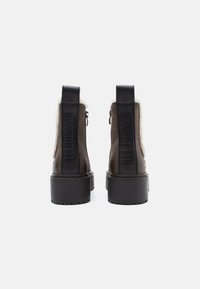 Par de botas de tobillo marrón oscuro con suelas gruesas negras, forro de piel de oveja visible en los bordes y branding "REPLAY" en las lengüetas traseras.