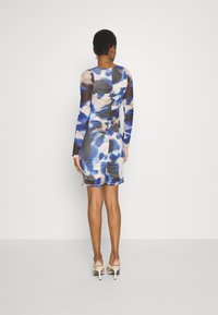 Robe mini à manches longues dans un motif abstrait bleu et beige, présentant une silhouette ajustée et des détails froncés au dos.