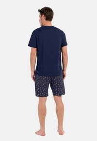 Navyblaues Baumwoll-T-Shirt, kombiniert mit navyblauen gemusterten Shorts, die kleine, hellfarbige Sternenexplosionen zeigen. Lässiger, entspannter Schnitt.