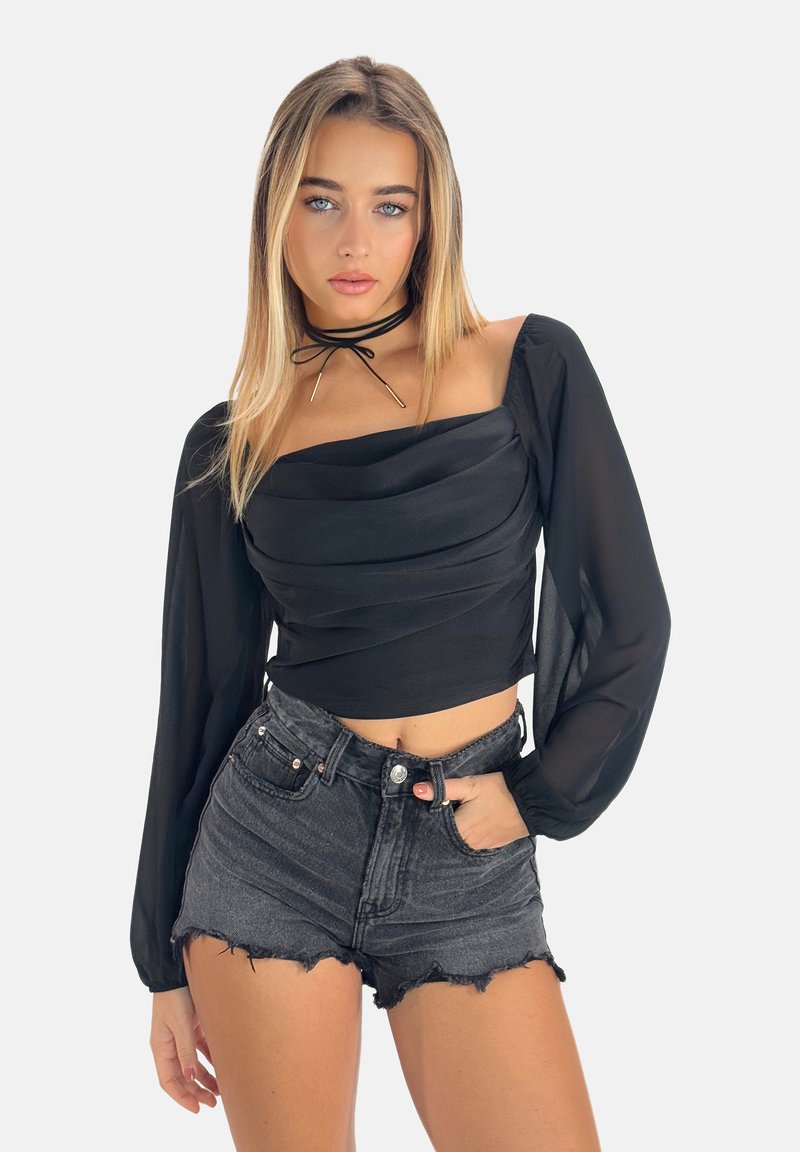 Zwarte cropped top met geplooide mouwen en geplooide details, gecombineerd met versleten zwarte denim shorts. Choker-accent voegt een stijlvolle touch toe.